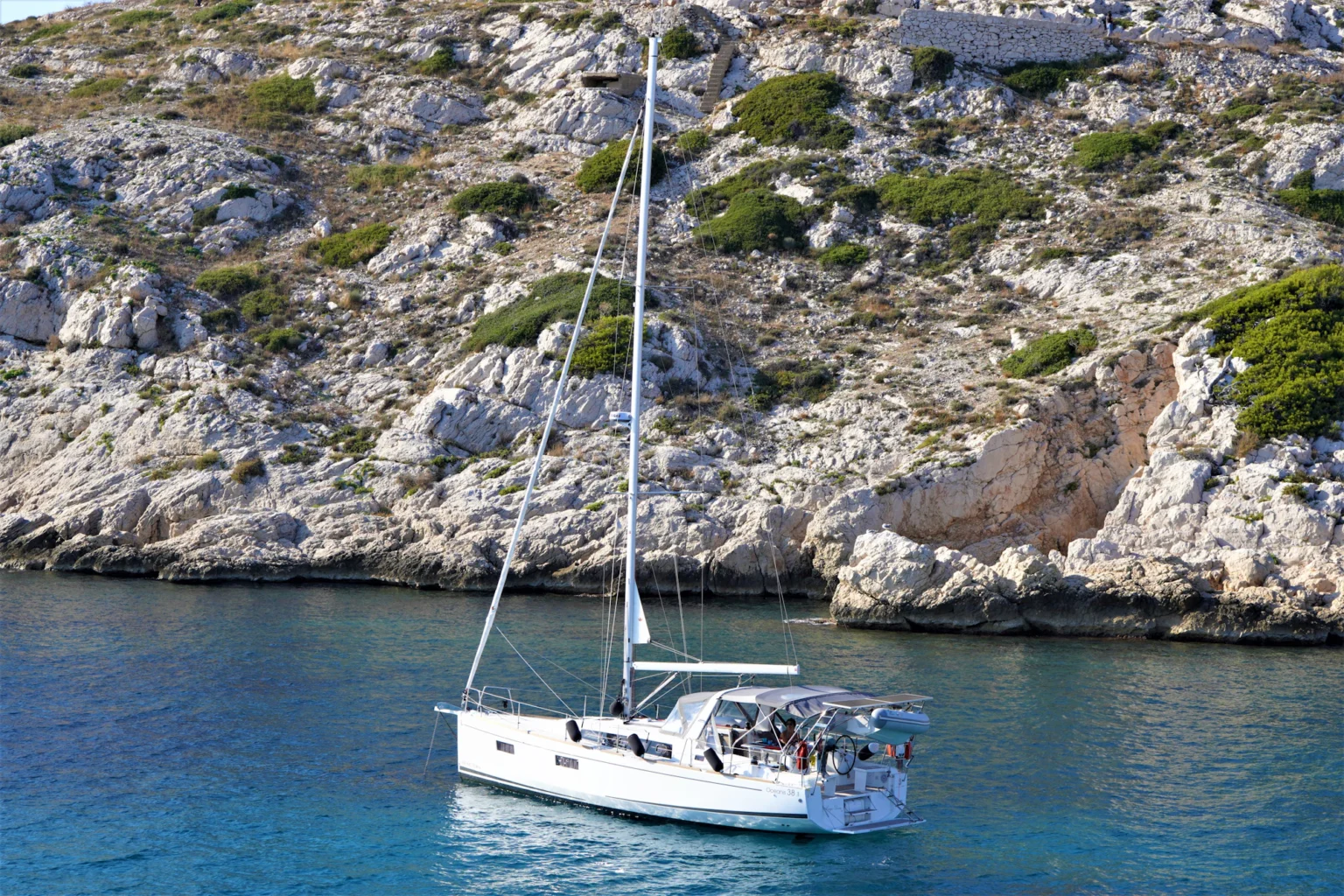 Sailing yacht at anchor below a rocky coast